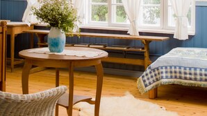 A cozy room with a wooden bench, a round table with a vase, and a bed with a checkered blanket. - Koivulan Kartano (Lohja)