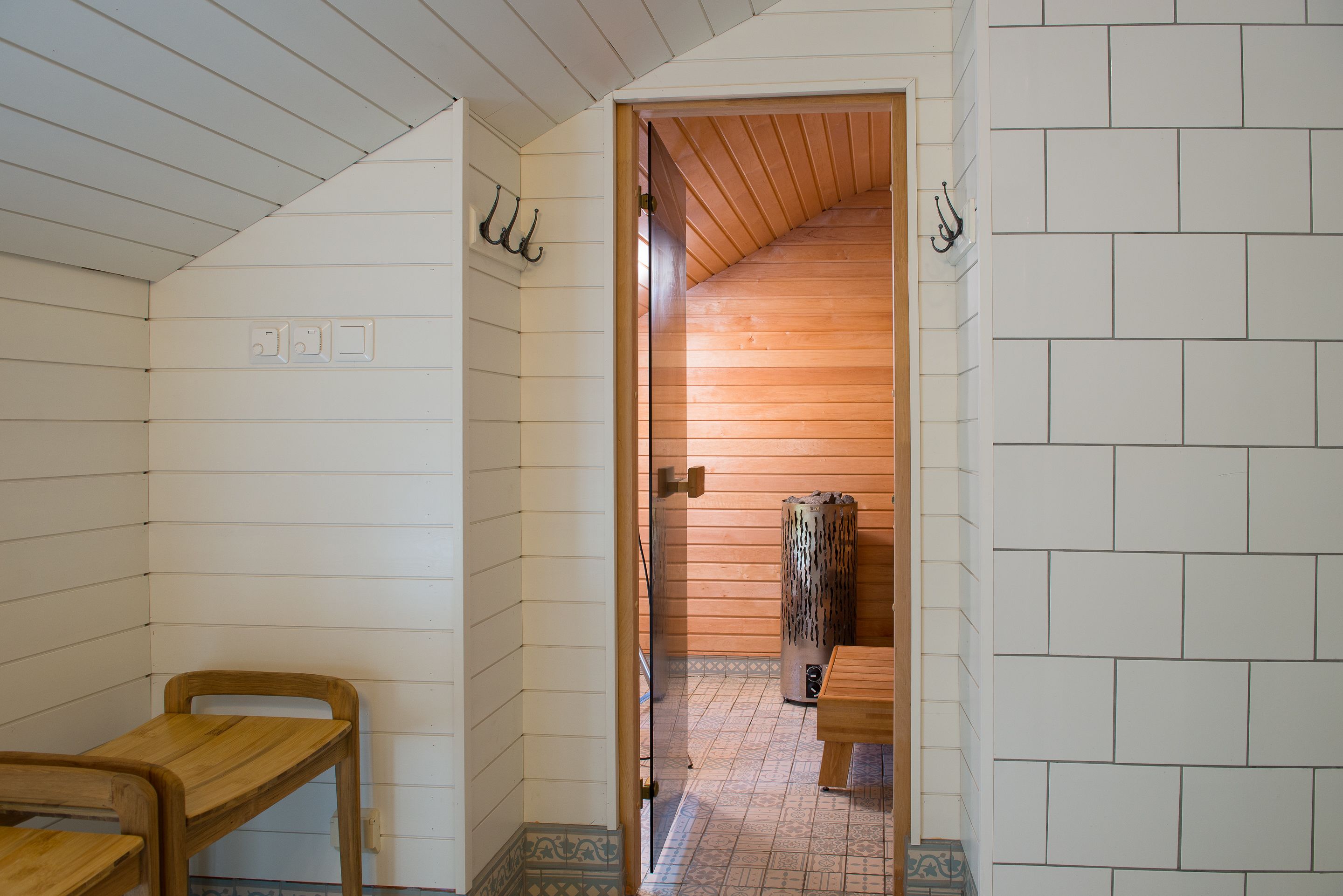 A room with a wooden ceiling, a wooden bench, a tiled floor, and a wooden wall with a towel hanging.