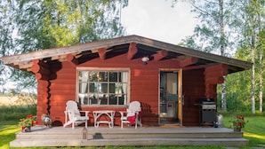 A rustic cabin with a porch, two Adirondack chairs, a table, and a grill. - Koivulan Kartano (Lohja)