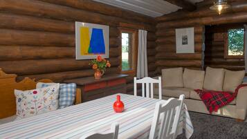 A log cabin interior with a dining table, chairs, a sofa, and a fireplace.