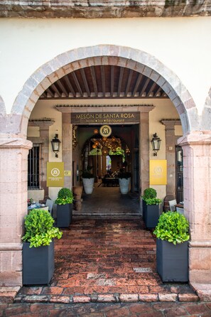 The entrance to Mesón de Santa Rosa, a hotel and restaurant with an arched brick facade, potted plants, and a signboard. - Mesón de Santa Rosa Luxury Hotel (Querétaro)