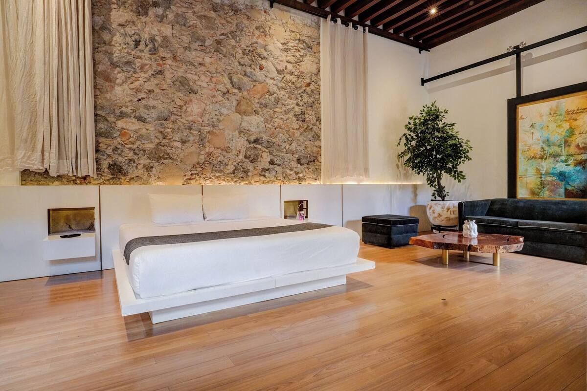 A modern bedroom with a stone wall, a large bed, a coffee table, and a sofa.