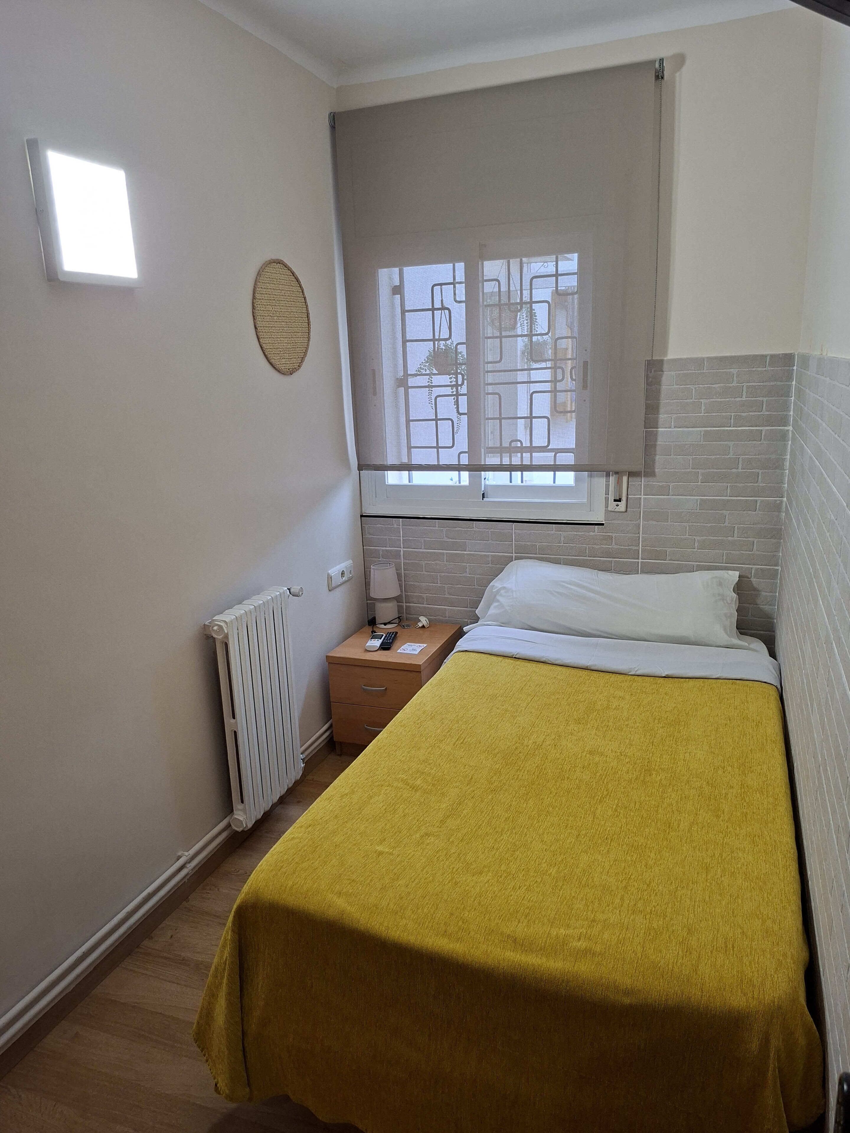 A bedroom with a bed, a nightstand, a lamp, a window with a view, and a radiator.