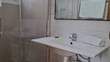 Een badkamer met een douchecabine van glas, een wit wastafelmeubel met een spiegel erboven en een radiator eronder.