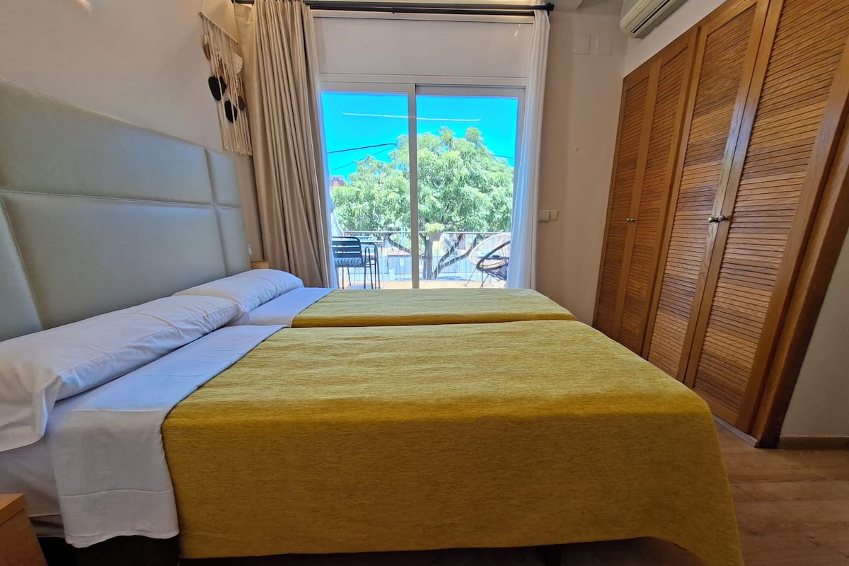 A room with a bed, a wooden wardrobe, and a view of the outdoors.