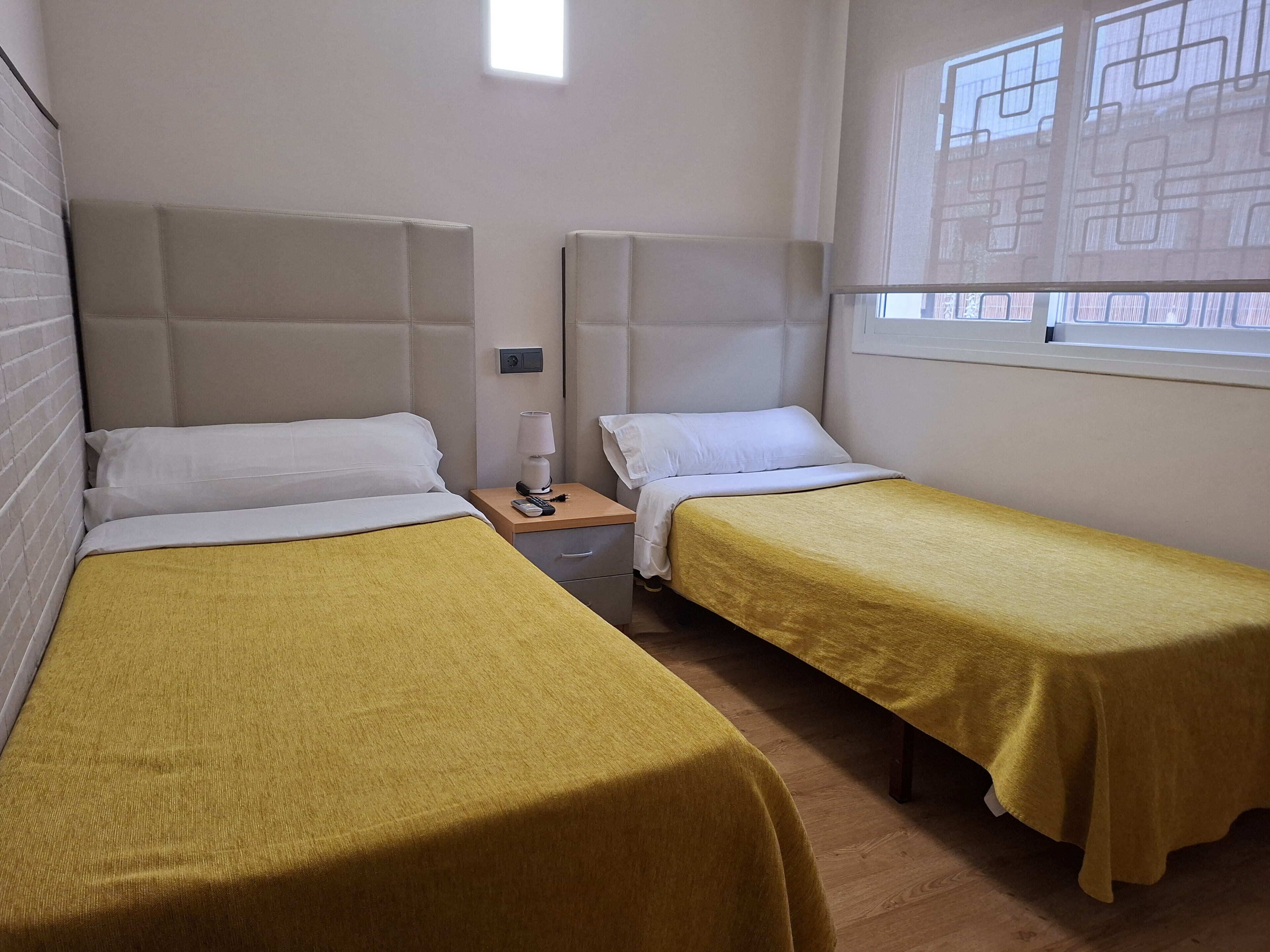 Una habitación con dos camas, una mesita de noche con lámpara y una ventana con vistas.