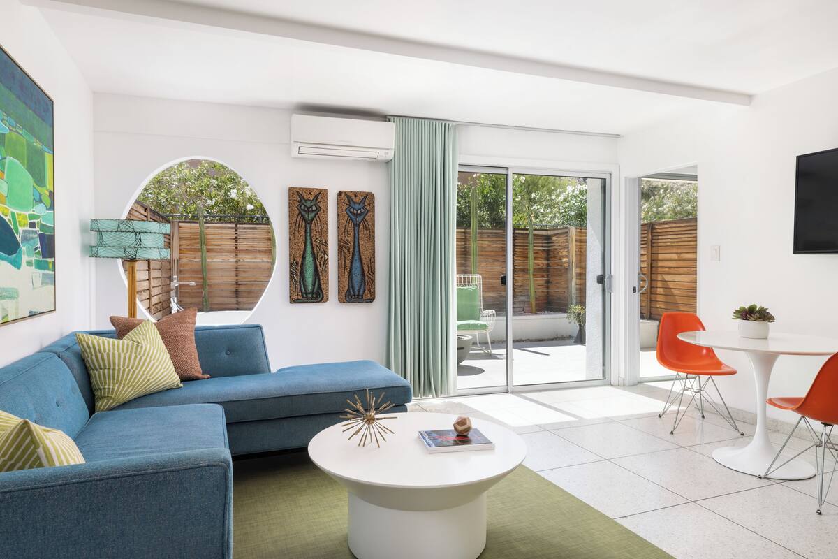 A modern living room with a blue sofa, white coffee table, and orange chairs.