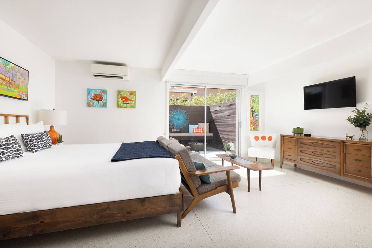 A modern bedroom with a large bed, a wooden chair, a small table, a TV, and artwork on the walls.