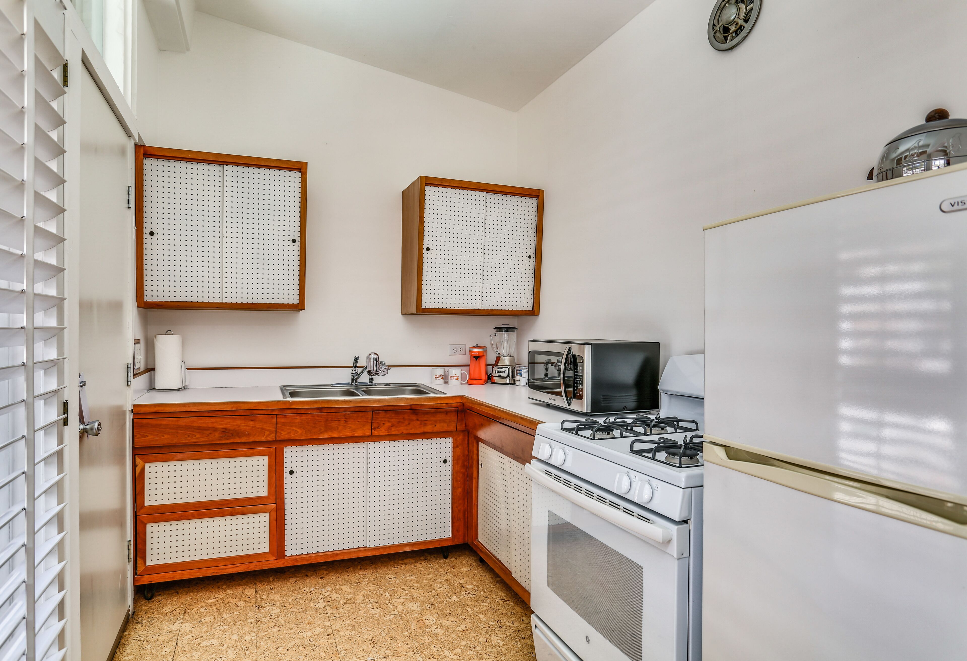 A kitchen with a white refrigerator, stove, microwave, and wooden cabinets with pegboards.
