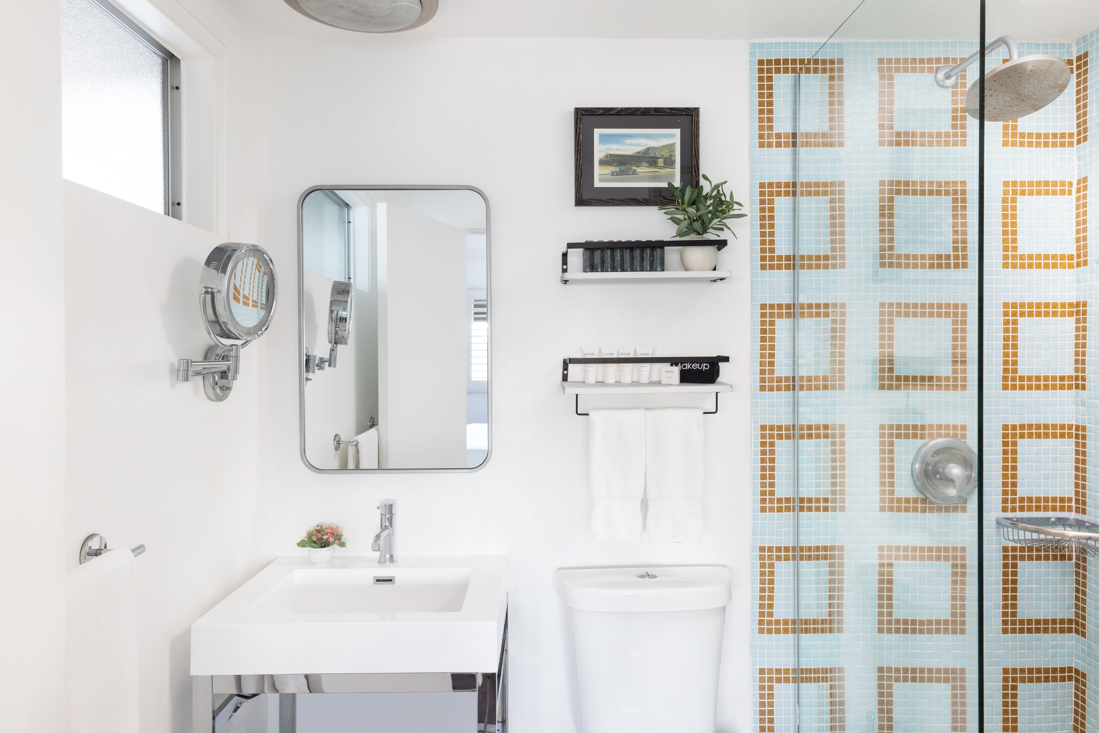 Un baño con lavamanos blanco, un espejo, un inodoro y una zona de ducha con azulejos estampados.