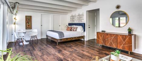 A modern bedroom with a bed, a dining table, chairs, a glass coffee table, a wooden cabinet, and a round mirror.