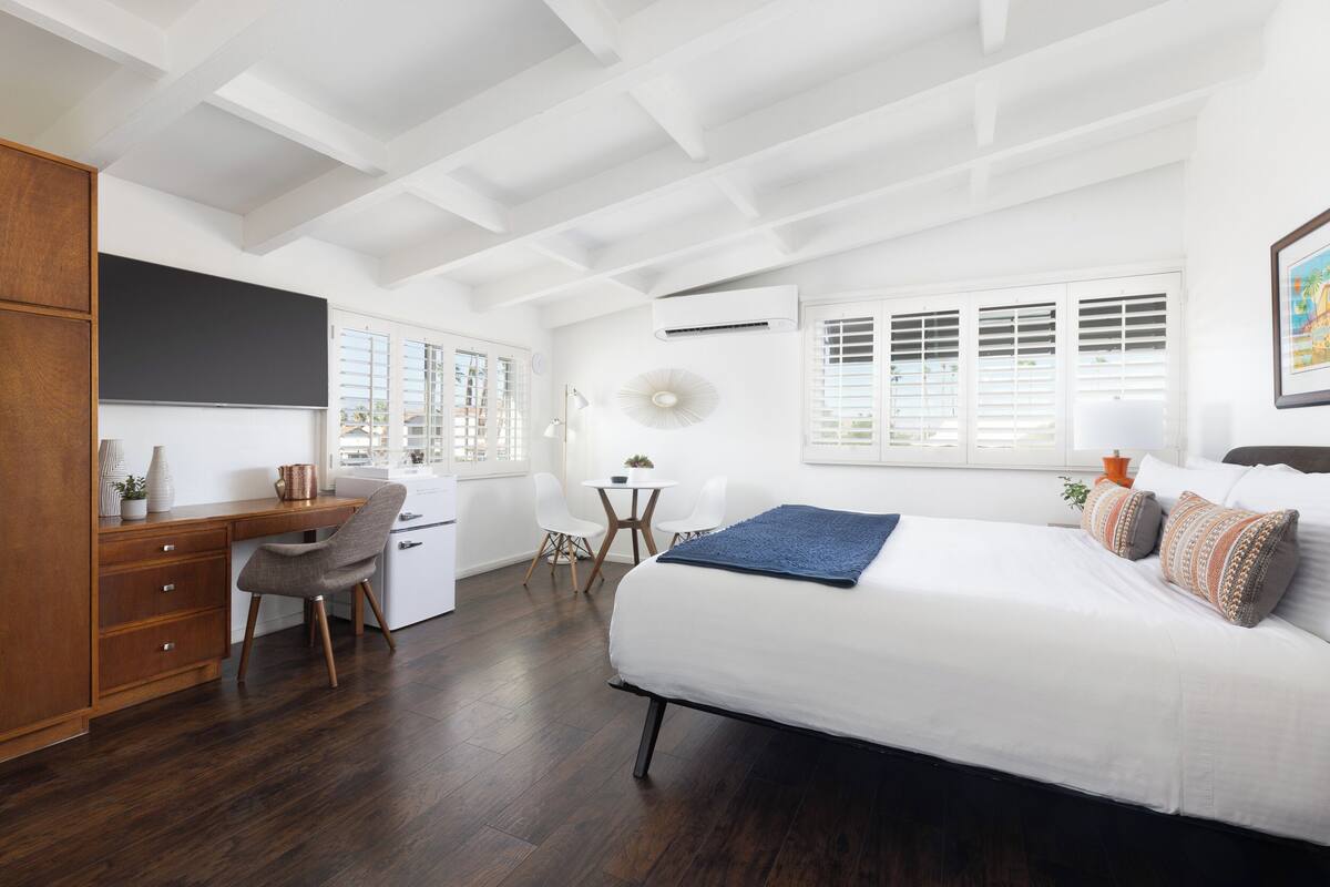 A bedroom with a bed, desk, chair, and a small table.