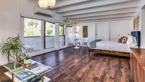 Un'ampia stanza con un letto grande, un tavolo da pranzo con sedie, un tavolino con riviste e una grande finestra vista palme.