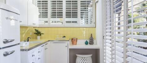 A compact kitchen with white cabinetry, a small countertop, and a window with blinds.