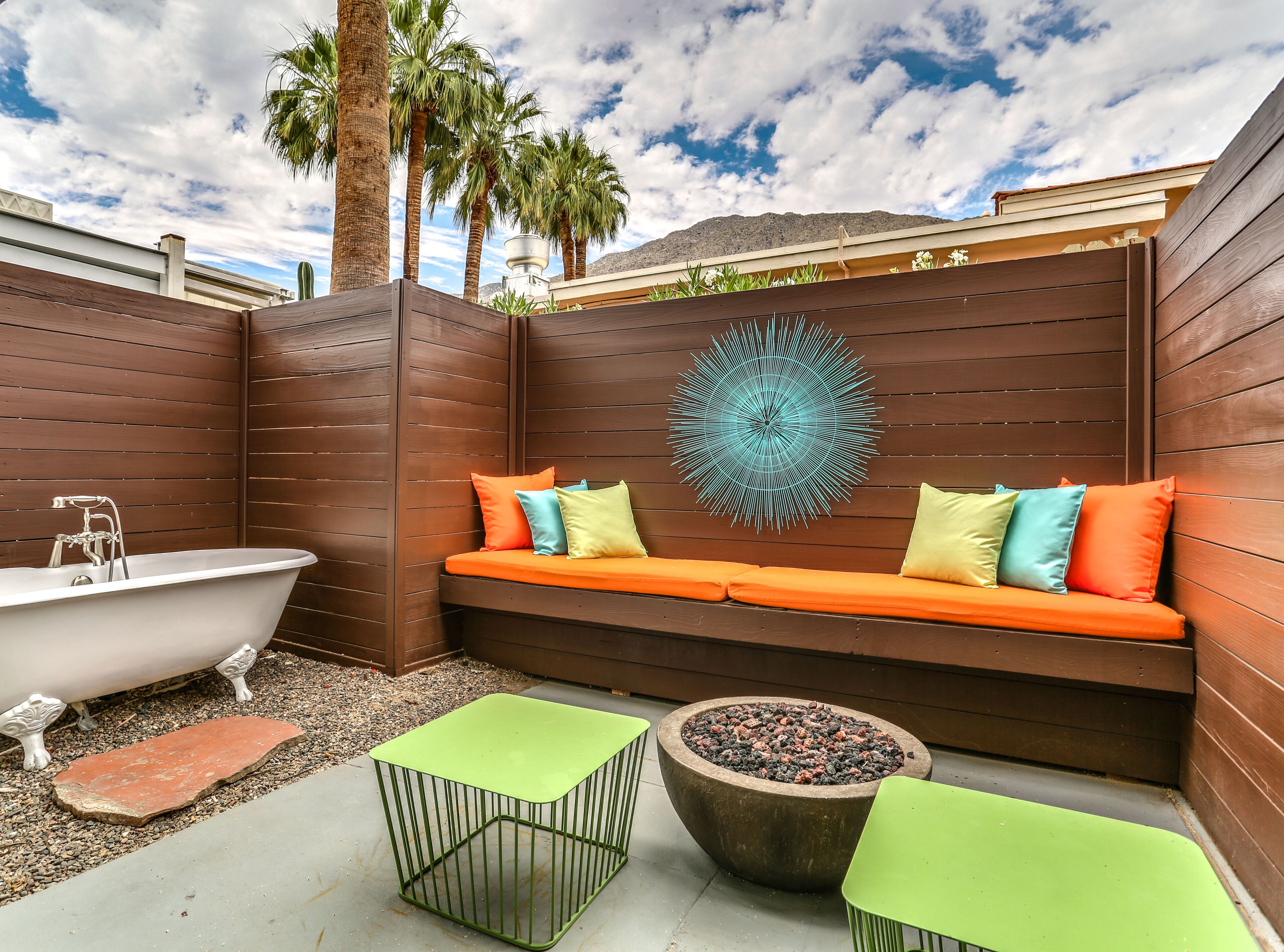 Una terraza de madera con una bañera, un pozo de fuego circular y un banco con cojines de colores.