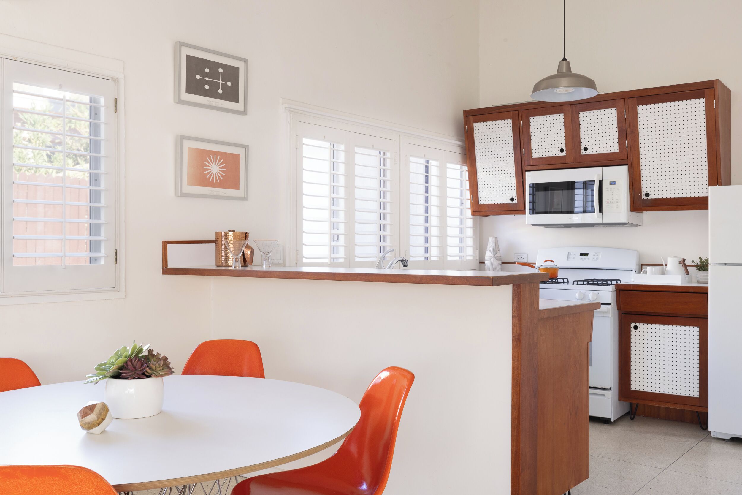 A kitchen with a white island, orange chairs, a white stove, and wooden cabinets.