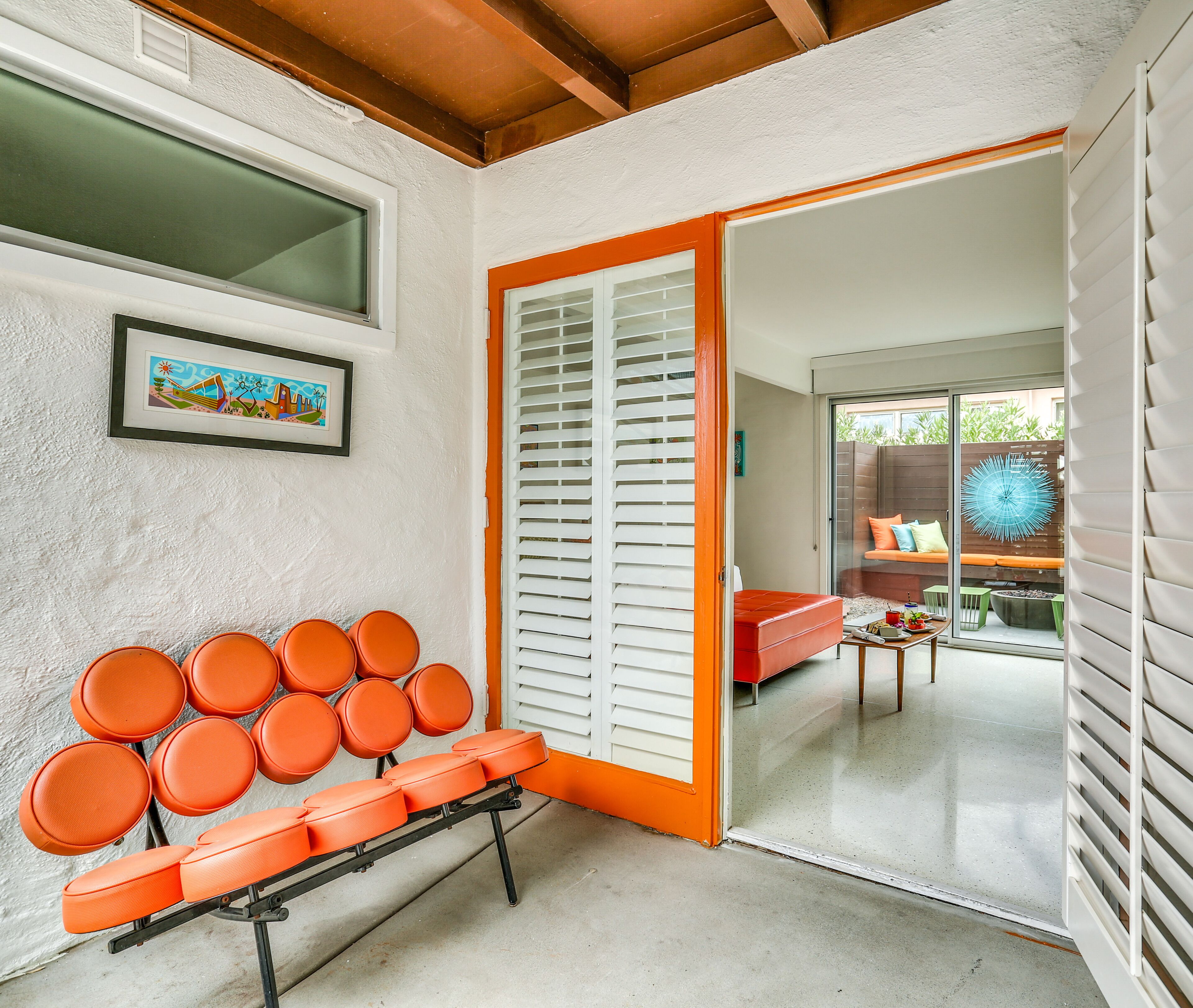 A room with a bench, a door, and a view of an outdoor seating area.