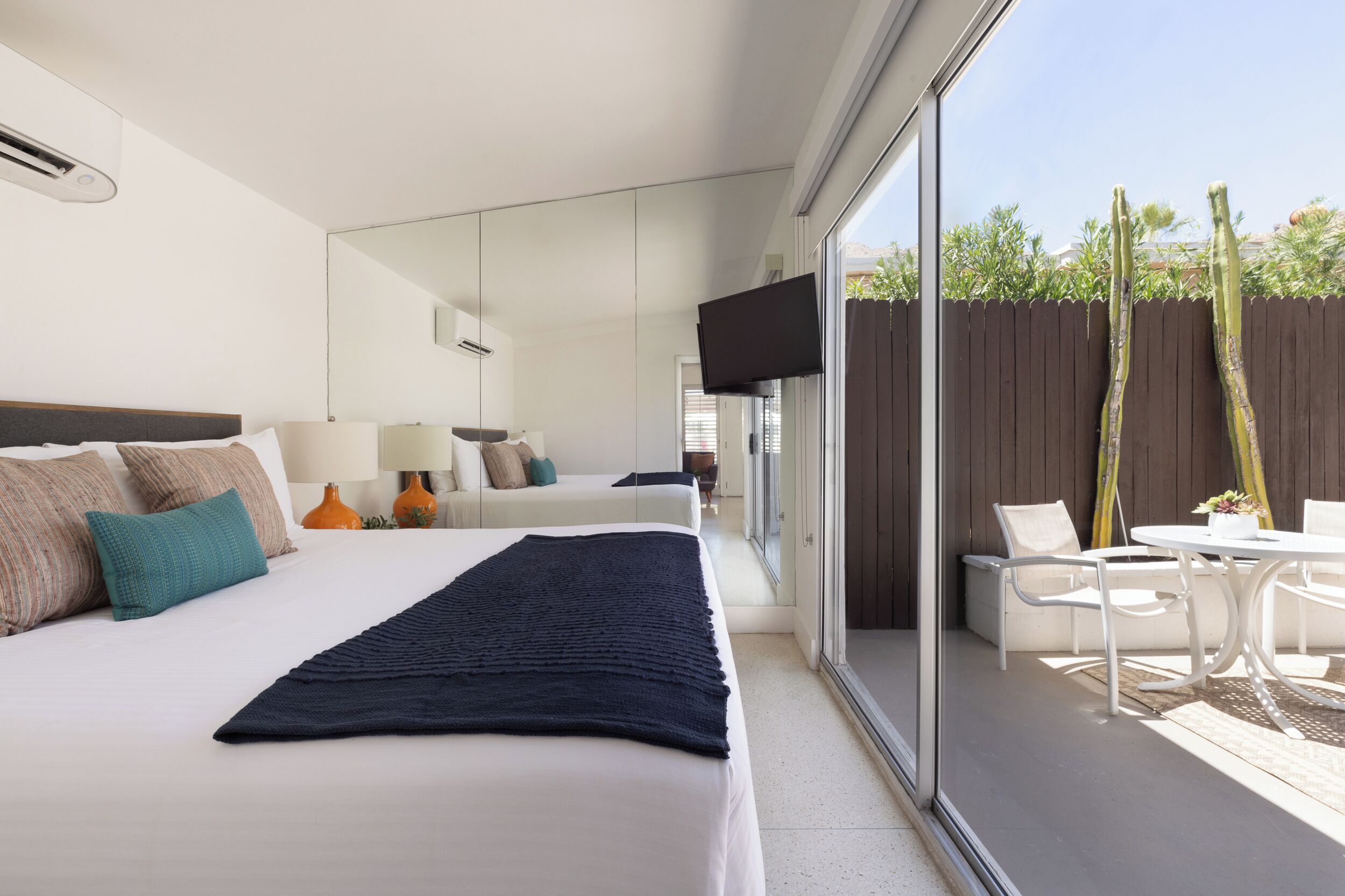 A modern hotel room with a large bed, a TV, and a balcony with outdoor furniture.