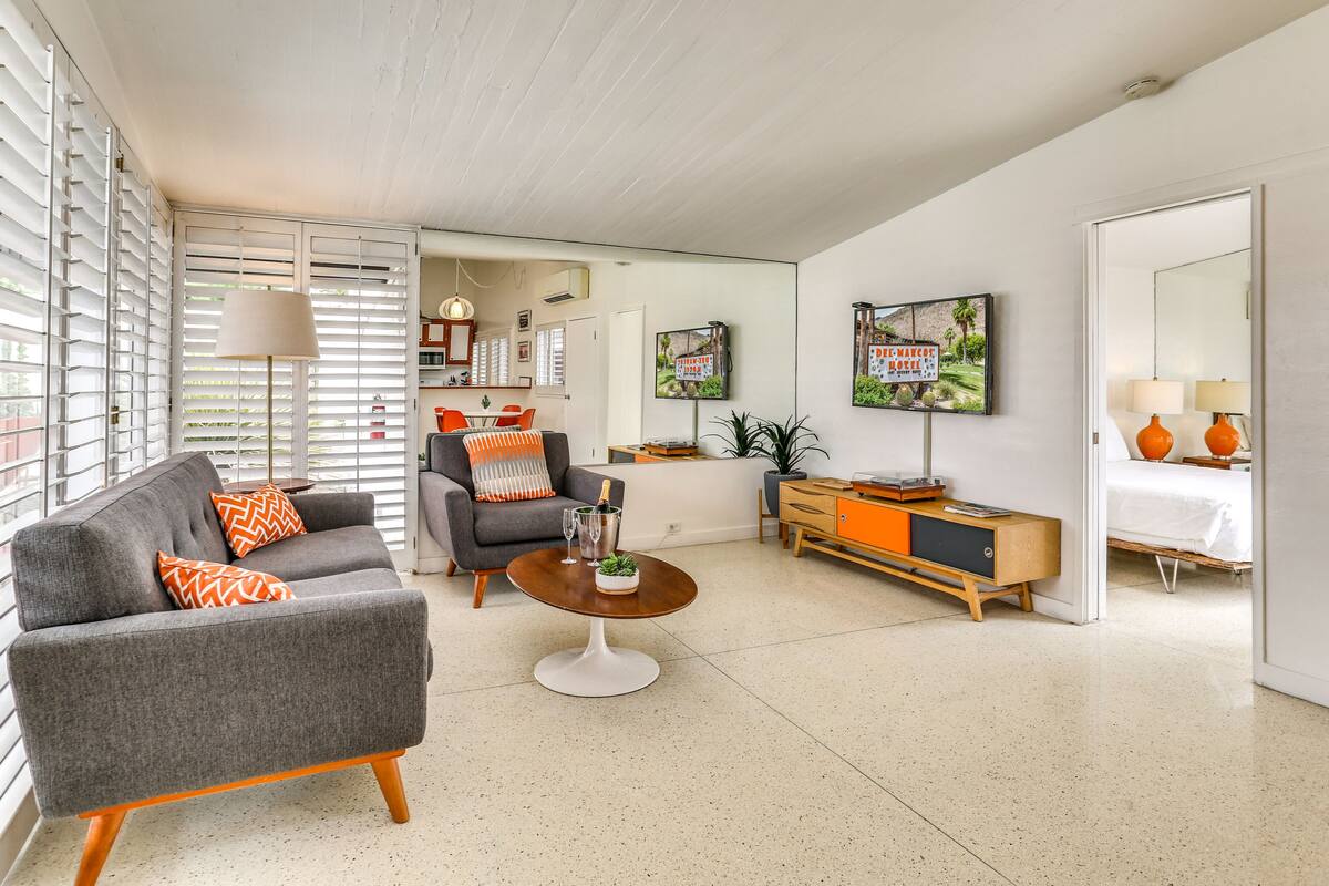 A modern living room with a grey sofa, orange patterned pillows, a wooden coffee table, and a TV on the wall.