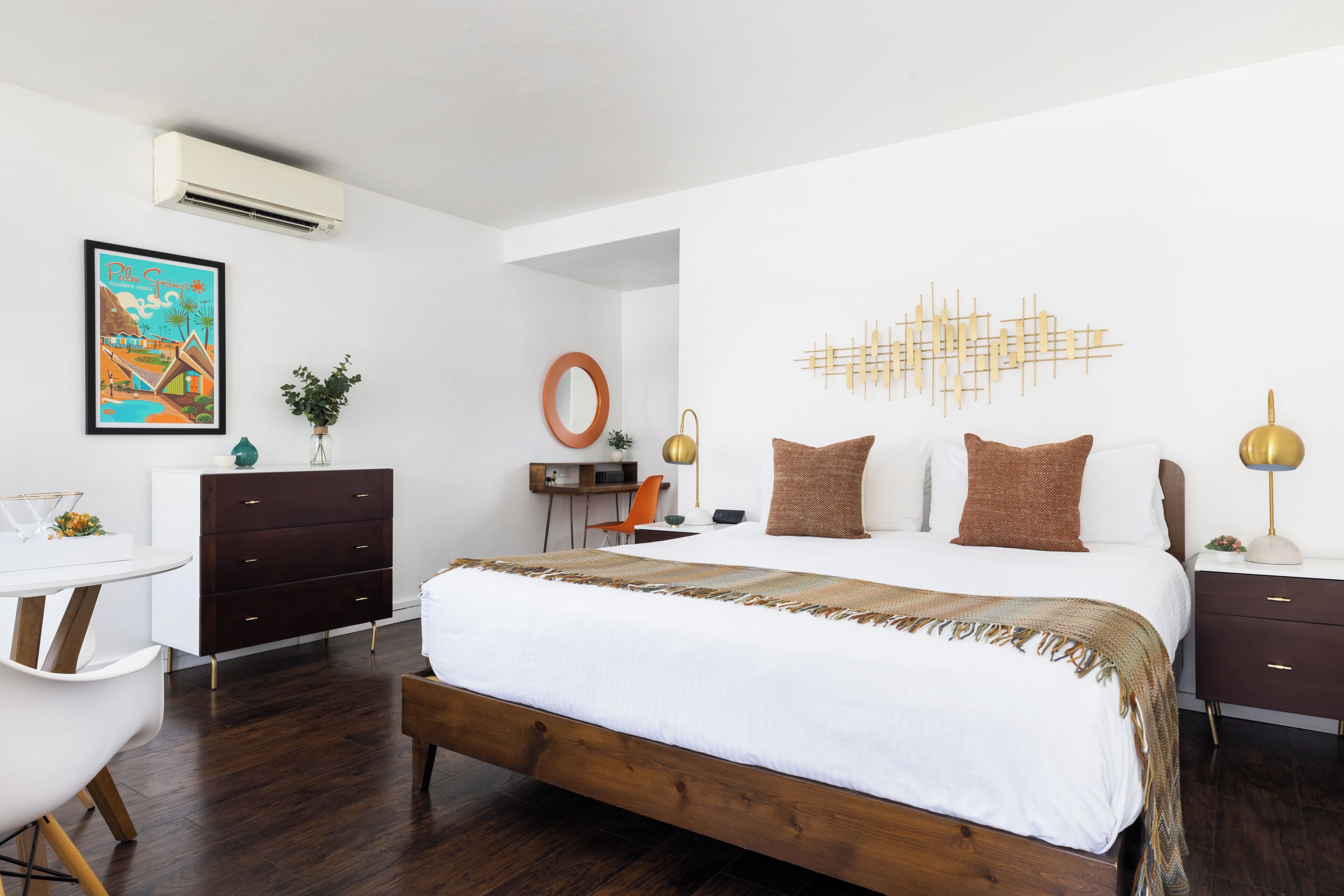 A modern hotel room with a large bed, a desk, and a chair. There is a wall-mounted air conditioner and a decorative wall piece.
