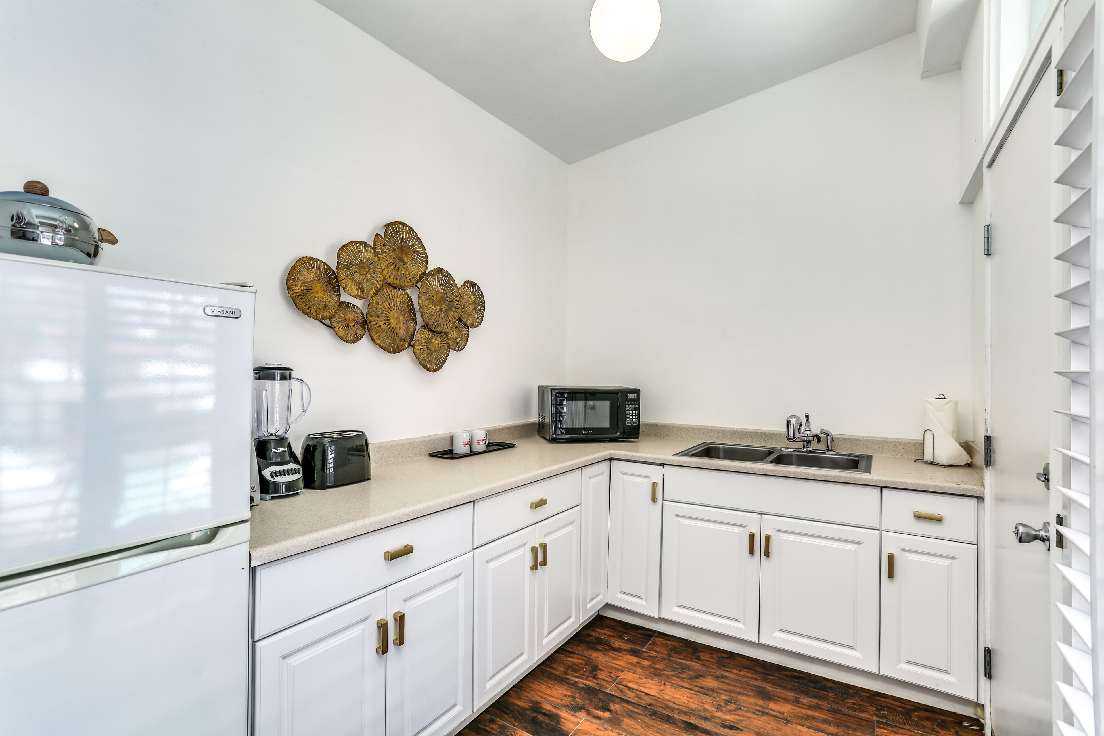 A kitchen with white cabinets, a refrigerator, a microwave, a sink, and a coffee maker.