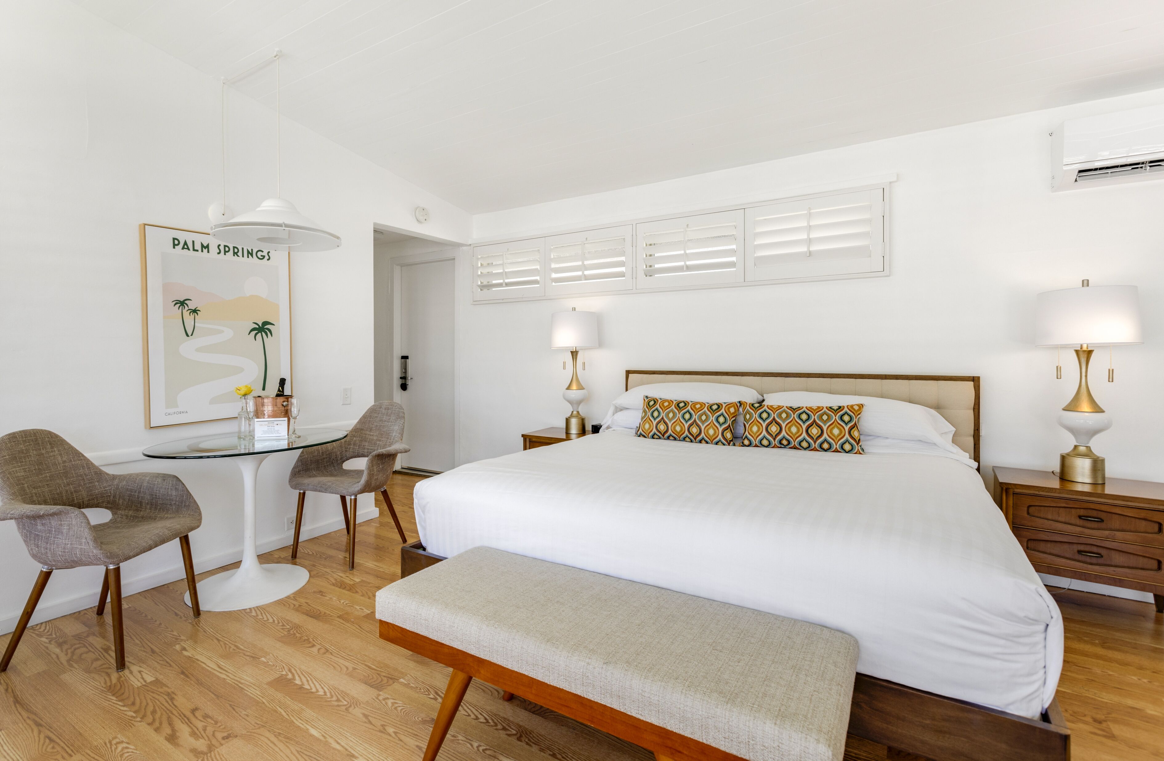 A bedroom with a large bed, bedside tables, a desk with chairs, and a bench.