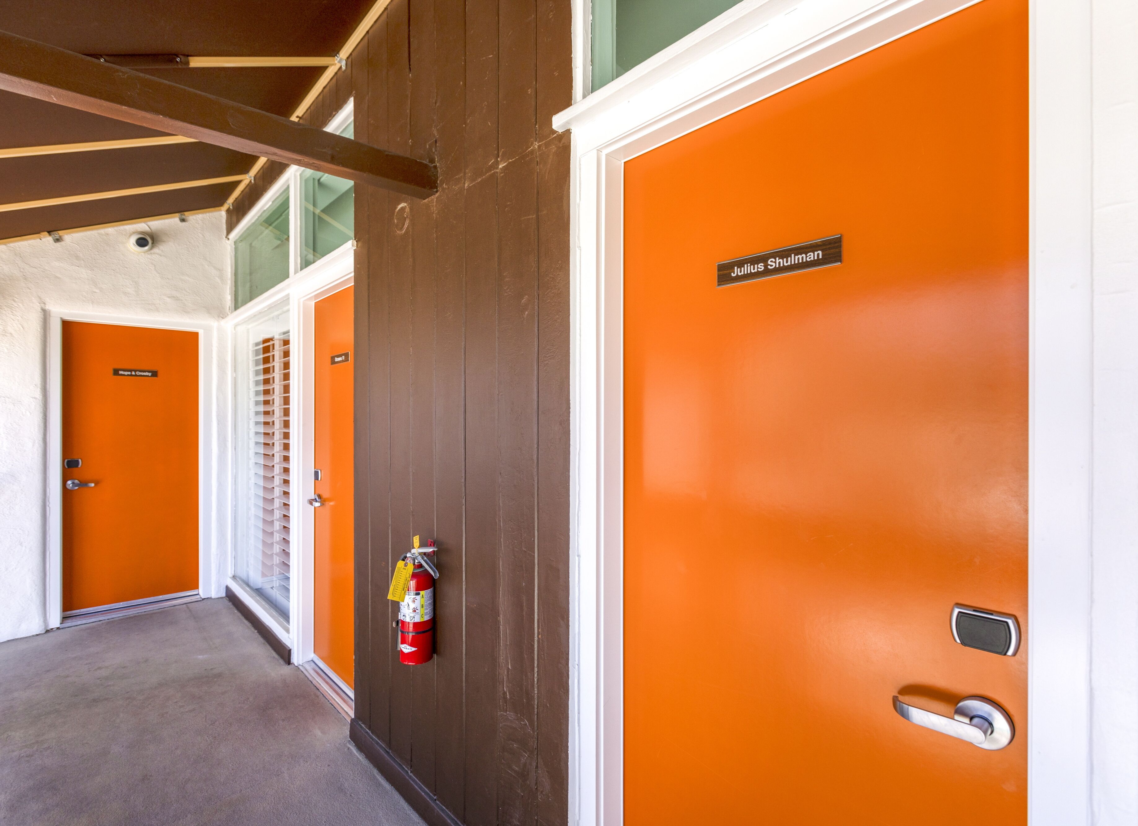Un pasillo con puertas naranja, un extintor y una placa identificadora en una puerta.