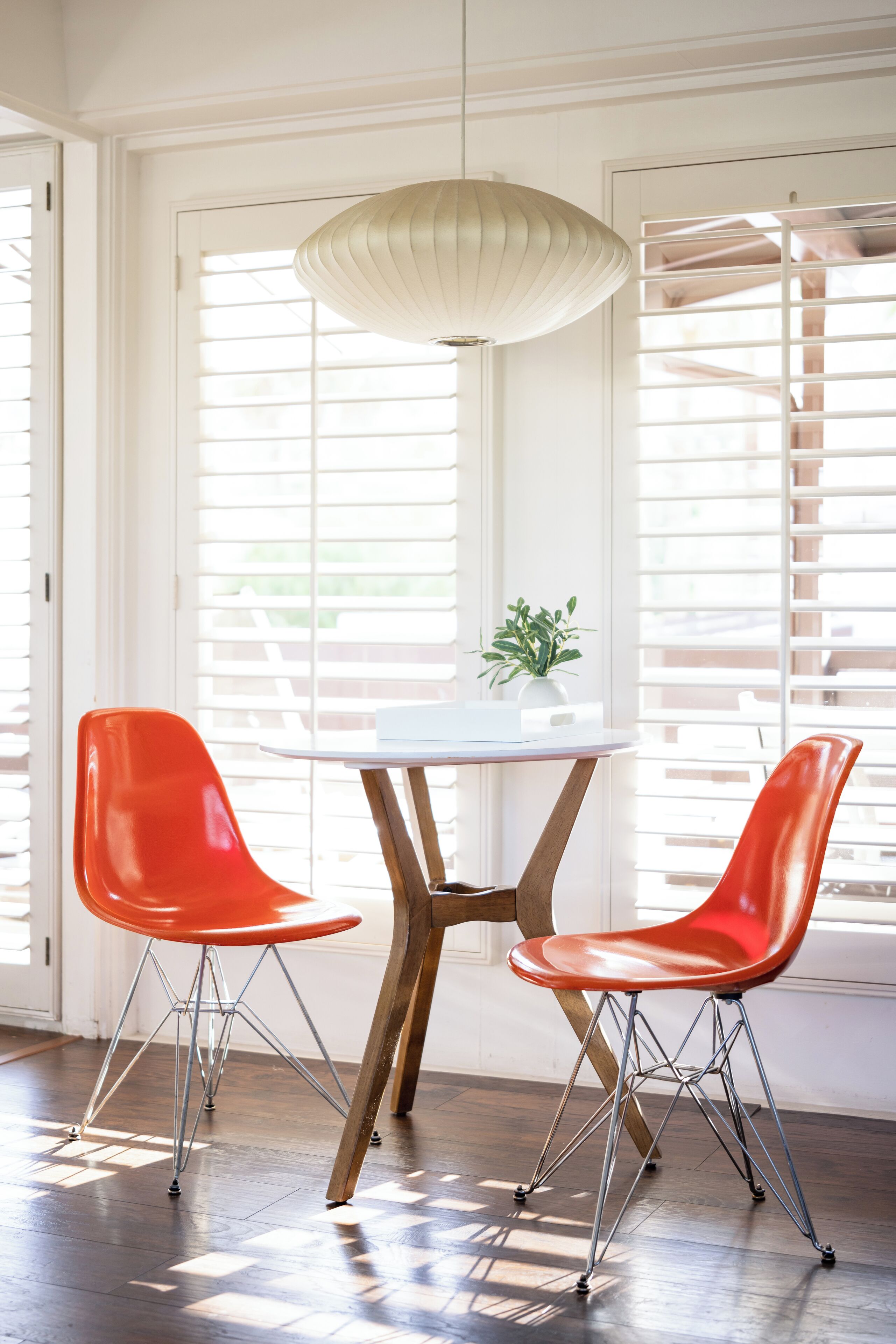 A dining area with a white table and two red chairs, a pendant light, and a potted plant.