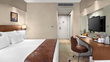 A hotel room with a bed, a desk with a chair, a television, and a small kitchenette area.