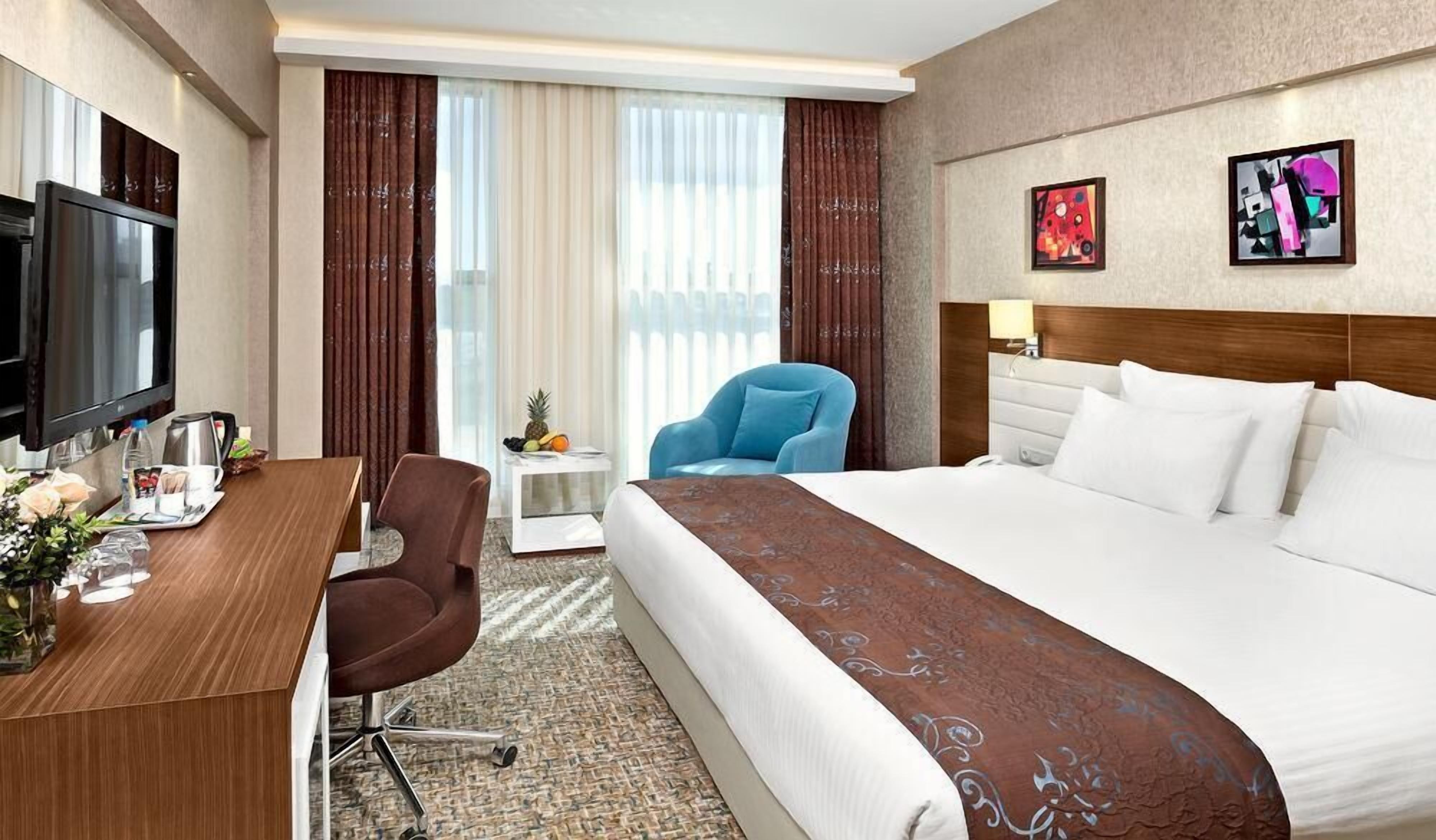 A hotel room with a bed, a desk, a chair, a TV, and artwork on the wall.