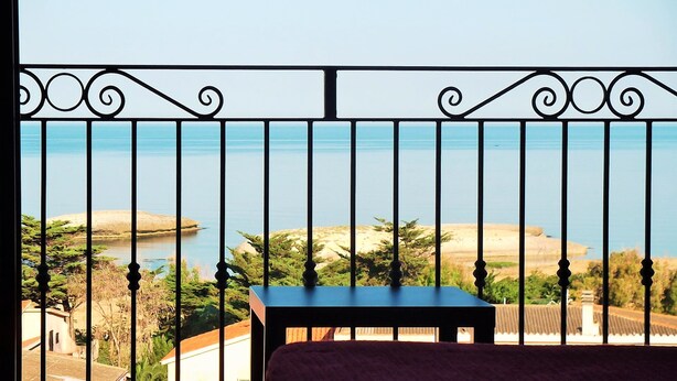 Un balcón con vista al mar, una mesa y algo de vegetación.
