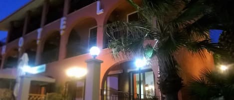 A hotel with a multi-story structure, arched balconies, and a palm tree in the foreground.