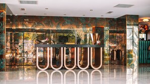 Ett välkomnande område med modern design, med en glasvägg som har ett tropiskt bladmotiv, en receptionsdisk och ett polerat golv.