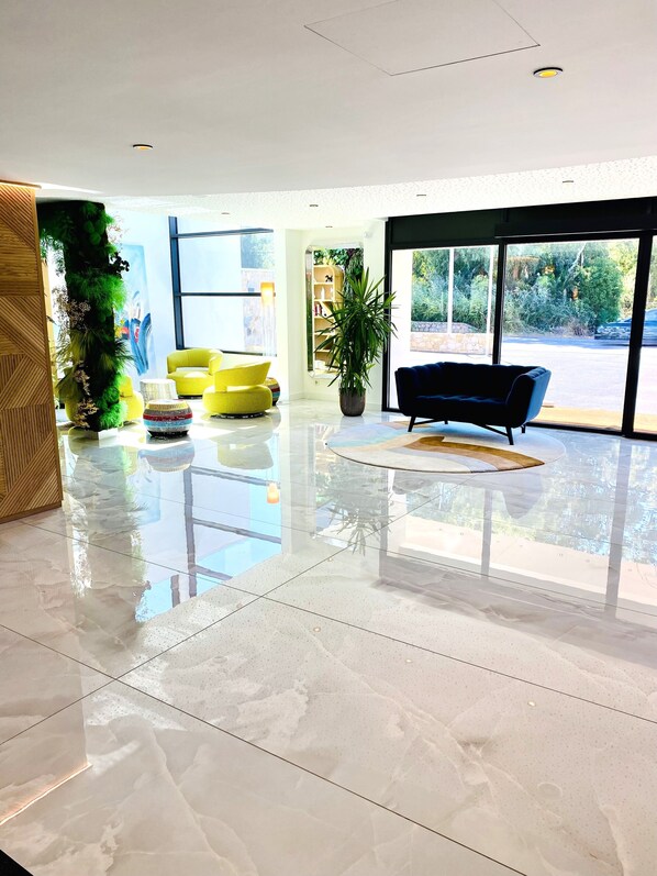A modern lobby with a glossy floor, a yellow armchair, a black sofa, and a large window offering a view of greenery. - Calvi Hôtel (Calvi)