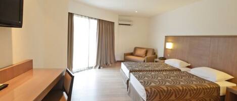 Habitación de hotel con escritorio, dos camas, televisión y ventana con cortinas.