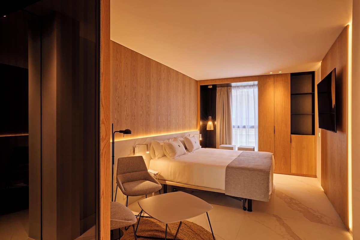 Une chambre d’hôtel moderne dotée d’un grand lit, d’un coin salon et d’un téléviseur fixé au mur.