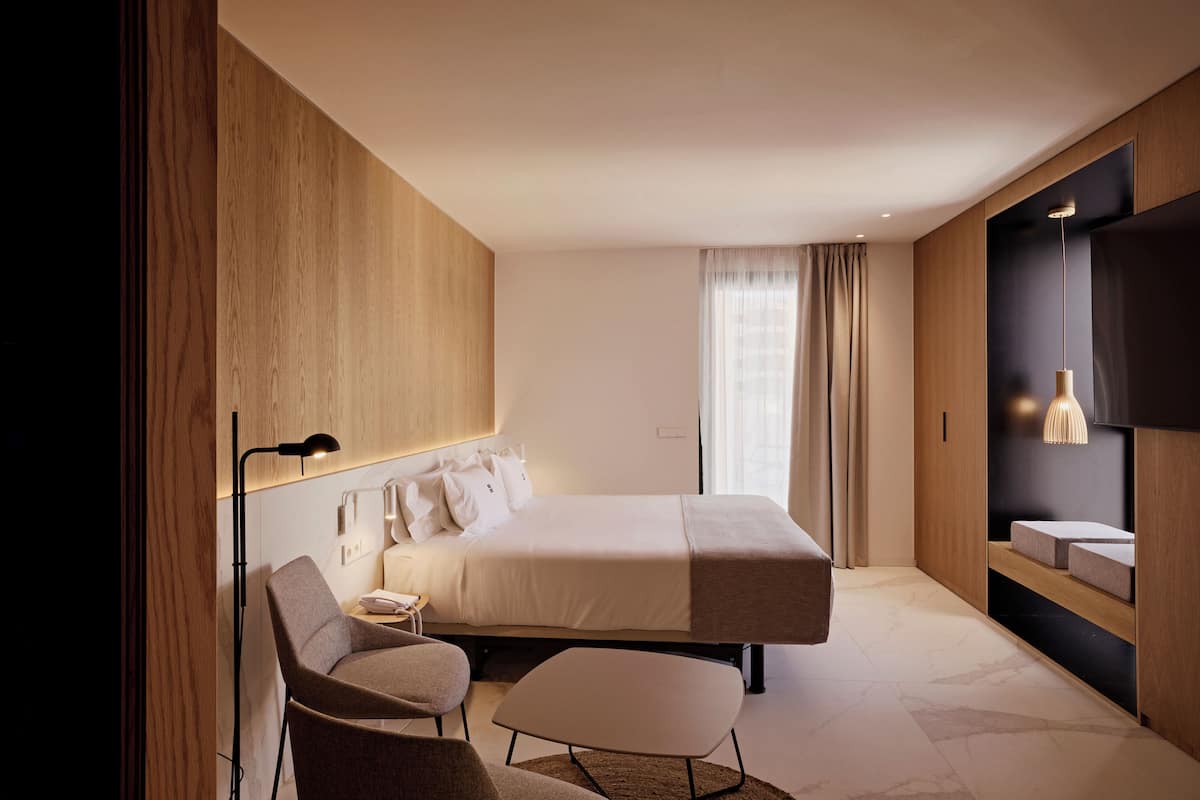Une chambre d’hôtel moderne dotée d’un grand lit, d’un bureau, d’une chaise, d’une télévision et d’une étagère intégrée avec un miroir.