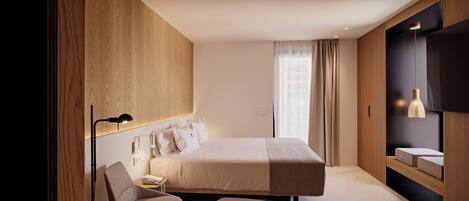 A modern hotel room with a large bed, a desk, a chair, a TV, and a built-in shelf with a mirror.