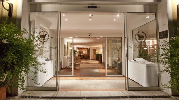 A hotel entrance with glass doors, a reception desk, and a visible dining area inside. - Hotel Das Goldene Lamm (Aalen)