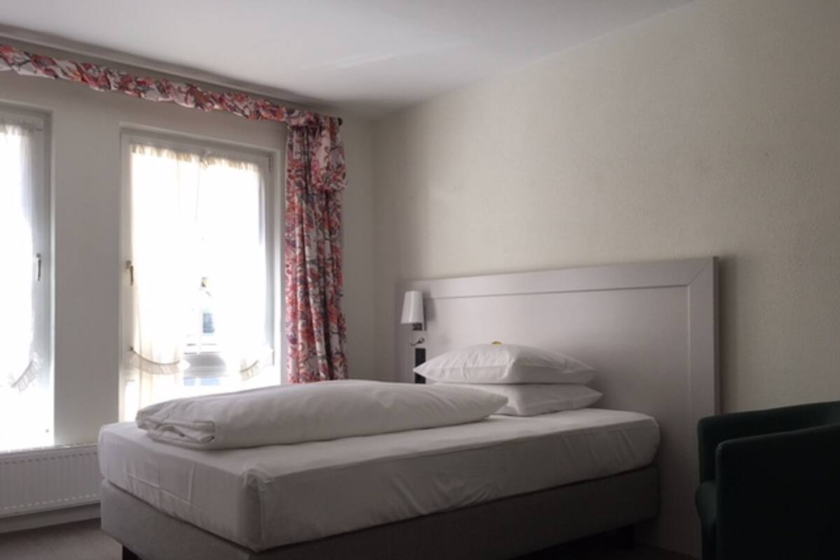 A bedroom with a bed, a nightstand, a lamp, and a window with floral curtains.
