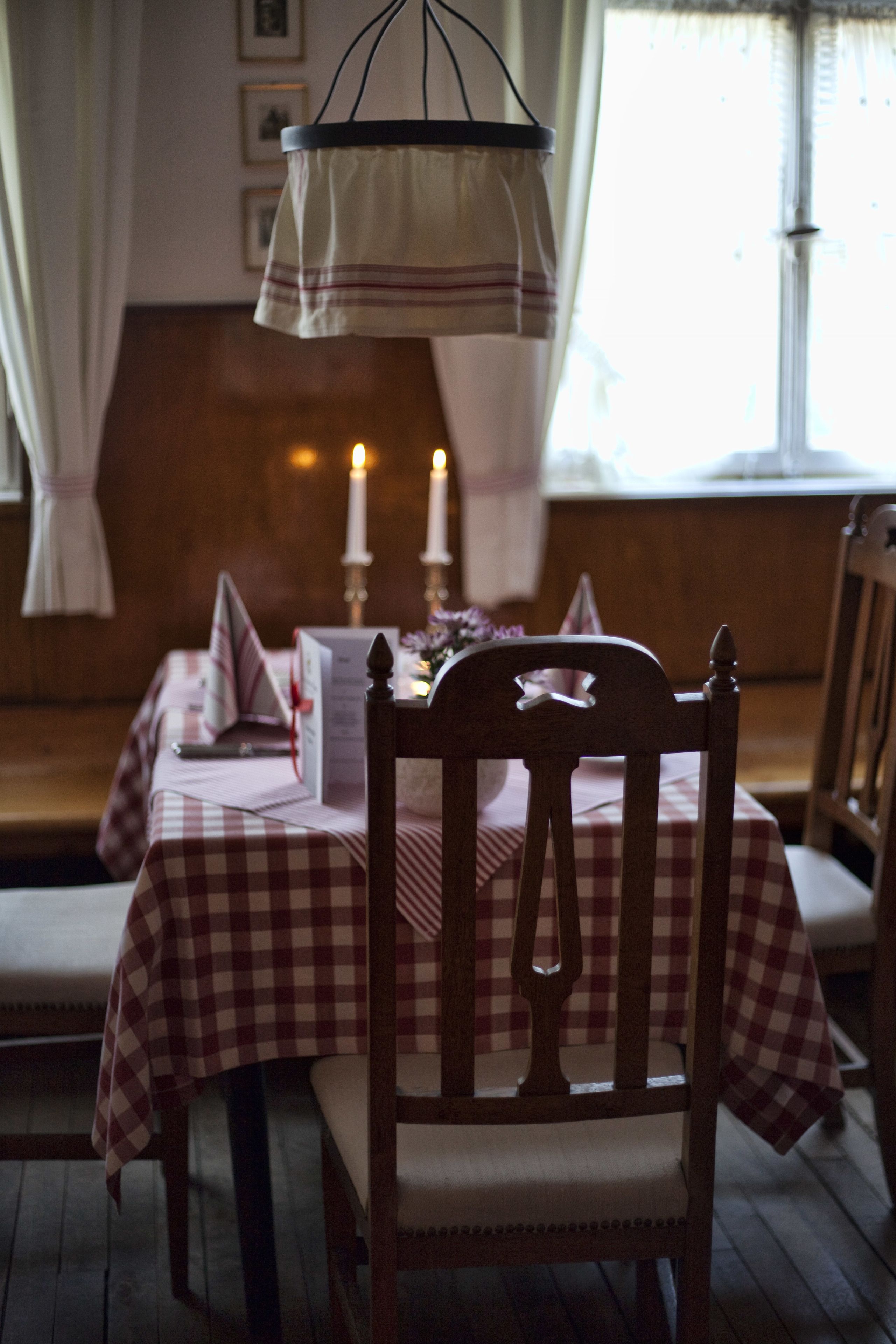 Un'area pranzo con tovaglia a quadri, sedie di legno, candele e un espositore per il menu.