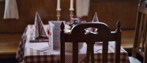 Un'area pranzo con tovaglia a quadri, sedie di legno, candele e un espositore per il menu.