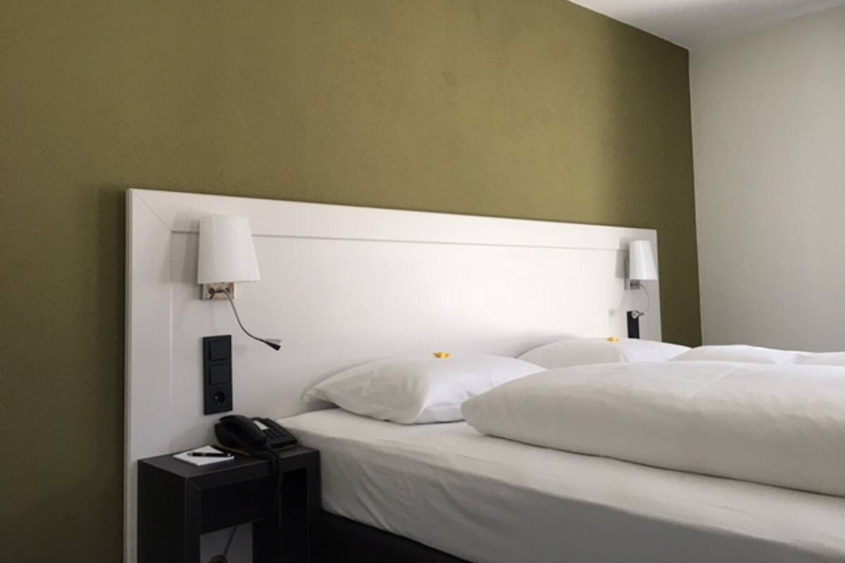 A hotel room with a single bed, a nightstand with a phone, and two wall-mounted lamps.