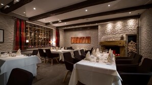 A restaurant with multiple tables set for dining, a fireplace, and a wine rack in the background. - Hotel Das Goldene Lamm (Aalen)