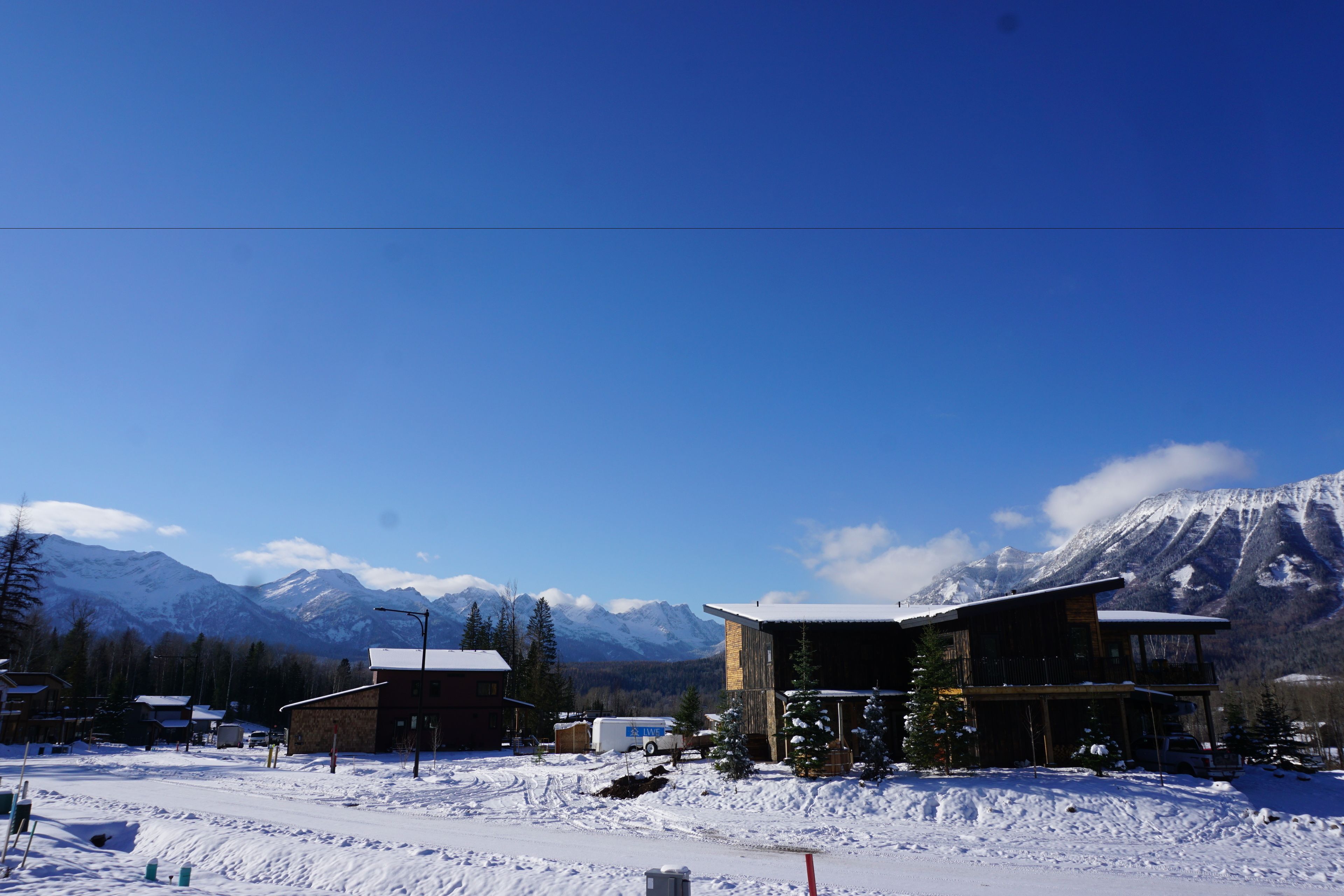 A snow-covered landscape with a mountain in the background, a wooden building with a balcony, and a clear blue sky.