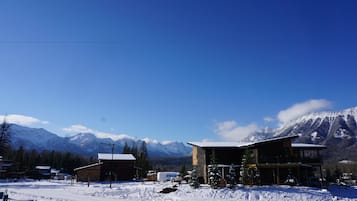 A snow-covered landscape with a mountain in the background, a wooden building with a balcony, and a clear blue sky.