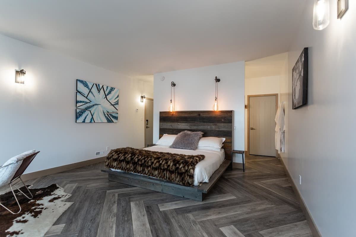 Un dormitorio moderno con cabecera de madera, una cama grande, un tapete de cuero de vaca y un cuadro abstracto colgado en la pared.