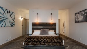 Un dormitorio moderno con una cama grande, cabecera de madera y dos lámparas fijadas a la pared.