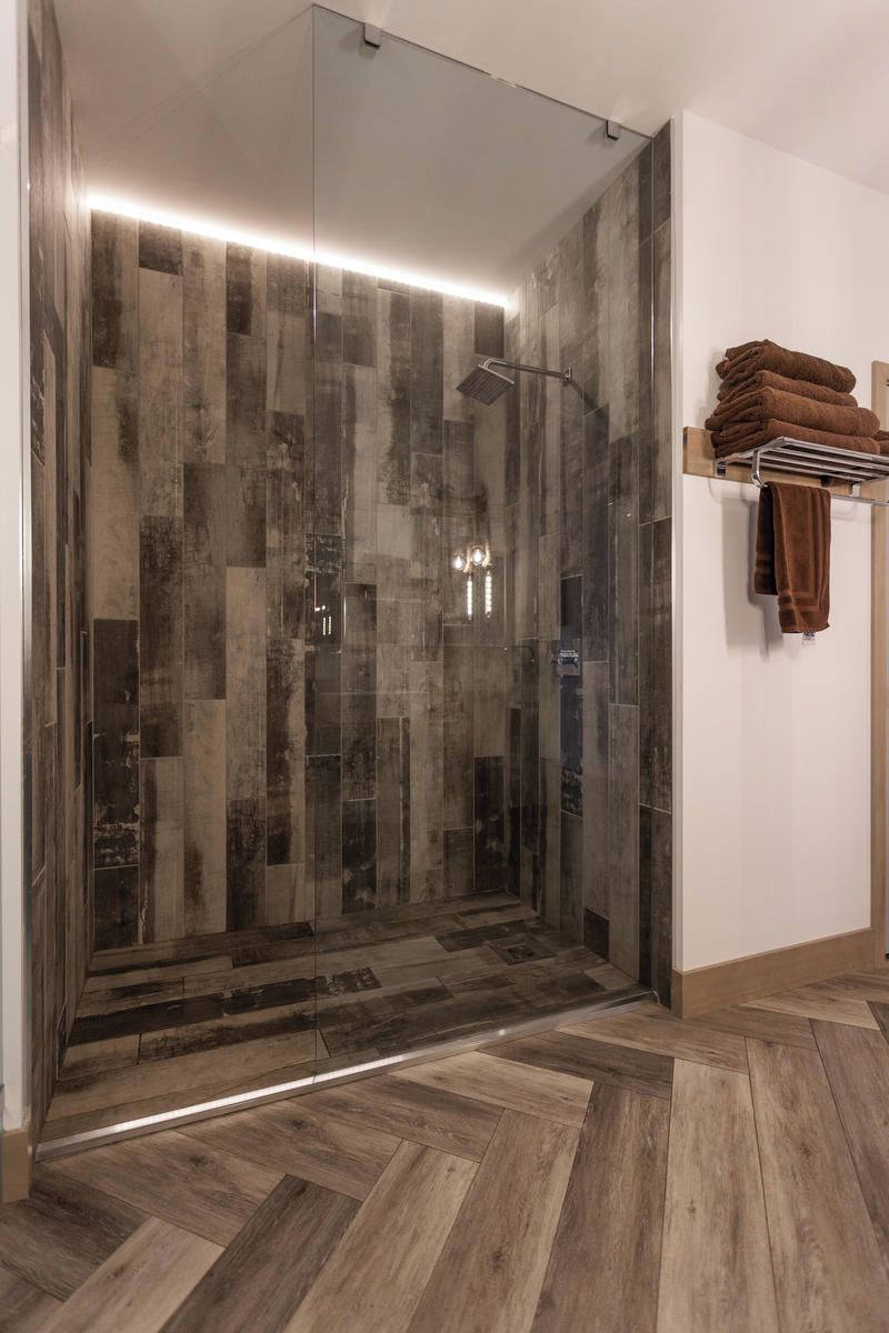 A modern bathroom with a glass shower enclosure, a wooden herringbone floor, and a towel rack with folded towels.