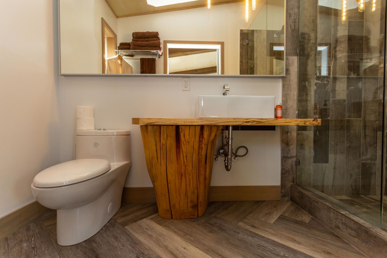 A modern bathroom with a wooden vanity, a toilet, and a glass shower enclosure.